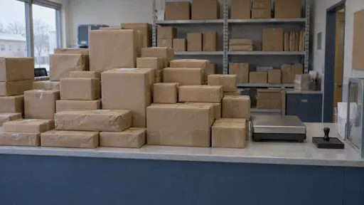 A tall stack of plain brown parcels has grown up from a post-office counter and spread across its whole front leaving a narrow clear strip with a blank scale and a stamp pad and shelves of more parcels behind in cool office light.