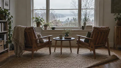 A woven rug is folded back neatly along one side to make space for a second wooden armchair set beside the first with both chairs facing a window and angled slightly toward each other with a low table between them in soft room light.