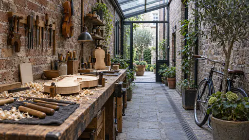 A violin maker's narrow bench runs along the wall of a brick side passage under a glass roof with clamps, a half-carved violin body and wood shavings on the bench and clear floor left for passing in cool daylight.
