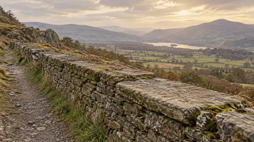A wide flat capstone worn smooth sits in a long dry stone wall beside a hillside path with moss and lichen on the stones and a sweeping valley view behind in warm golden light.