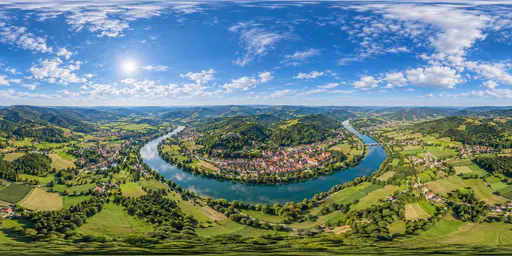 A full 360 degree equirectangular aerial panorama from high above a green river valley town with red roofed houses, a winding river, patchwork fields and forested hills with sky overhead.