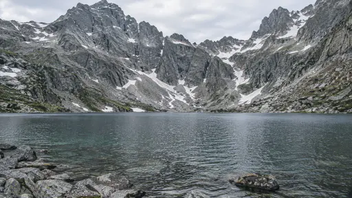 A cold mountain lake fills the basin beneath a steep rock cirque wall that rises directly from the far shore in clear alpine daylight.