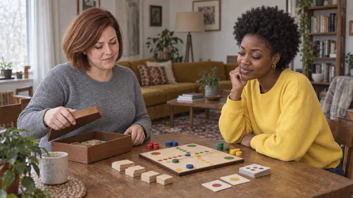 A woman with a chin-length auburn bob in a grey sweater lays out a wooden board game with coloured counters and tiles on a square table while a young woman with a short natural afro in a yellow sweatshirt leans in with a hand on her chin in warm light.