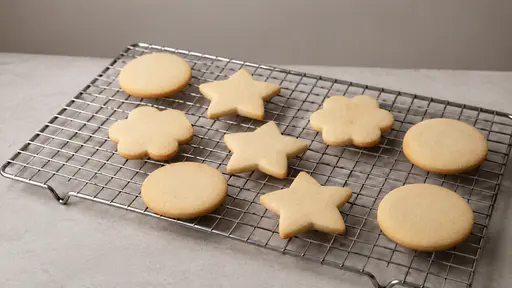 Plain uniced sugar cookies rest spaced apart on a plain wire cooling rack over a plain counter in bright even light.
