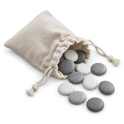 A small cotton drawstring bag on its side with a dozen smooth round grey and white counting stones spilling from its open mouth, on a transparent background.