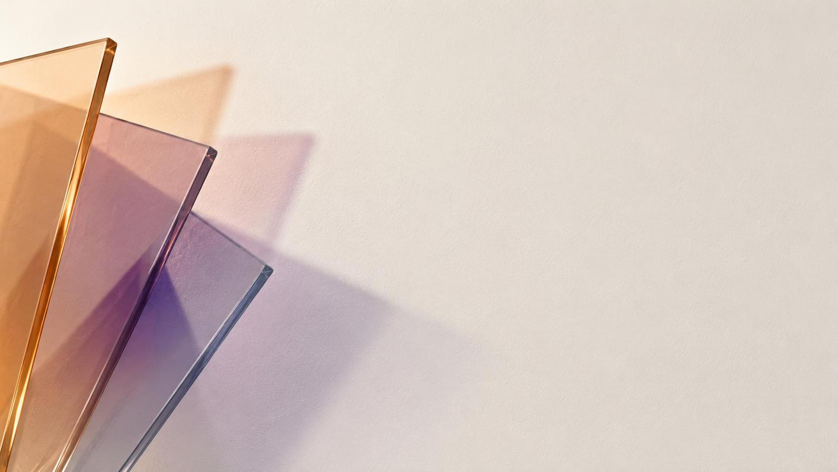 A fan of overlapping translucent glass sheets enters from the lower left corner throwing muted apricot and smoky lilac shadows across a blank ivory wall that fade before the centre, except at one small deep violet patch where three shadows cross and mix.