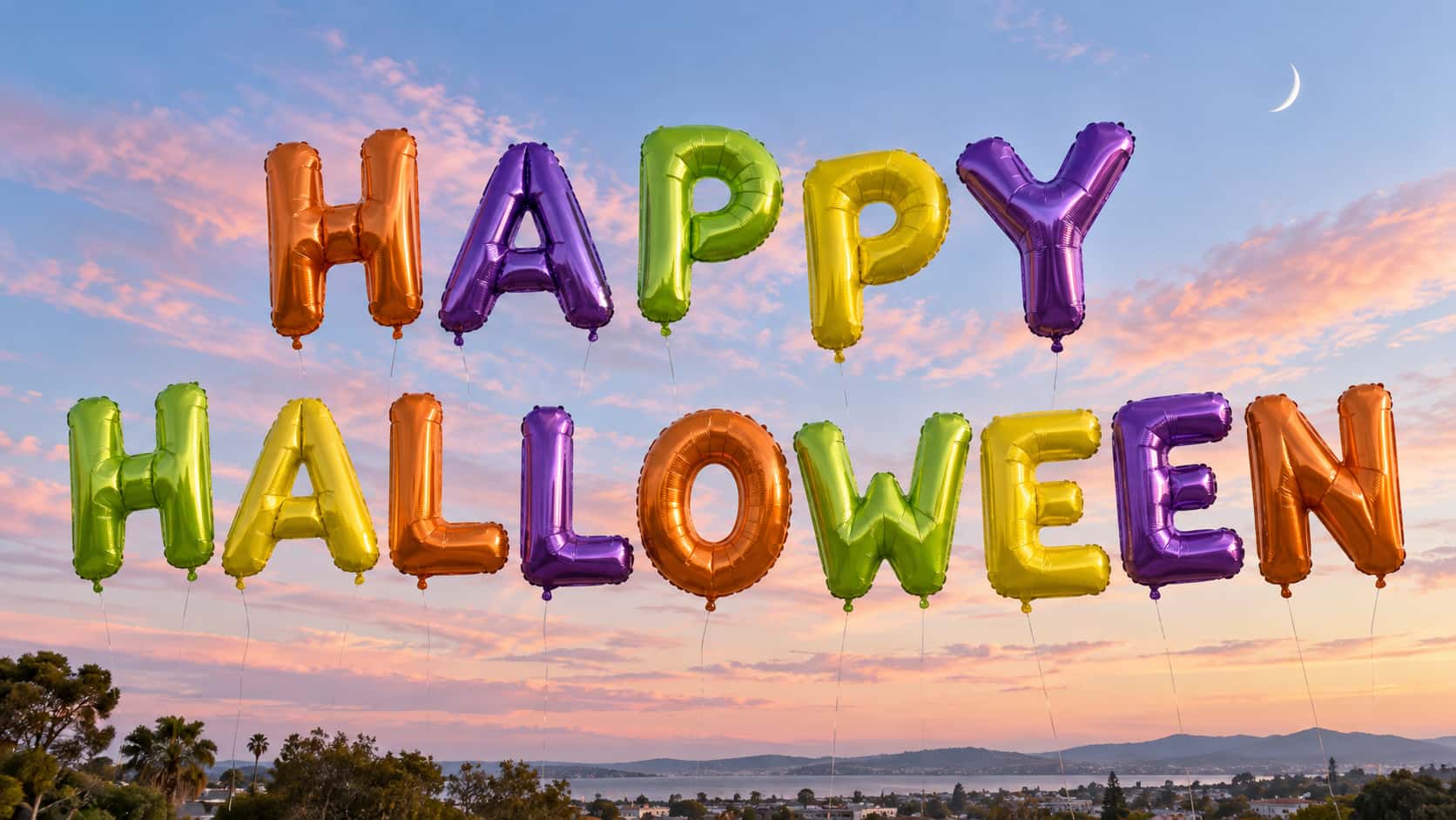 The words HAPPY and HALLOWEEN in two rows of glossy foil balloon letters in orange, purple, lime green and yellow floating in a pastel dawn sky with pink clouds and a thin crescent moon, a town, trees and a lake far below.