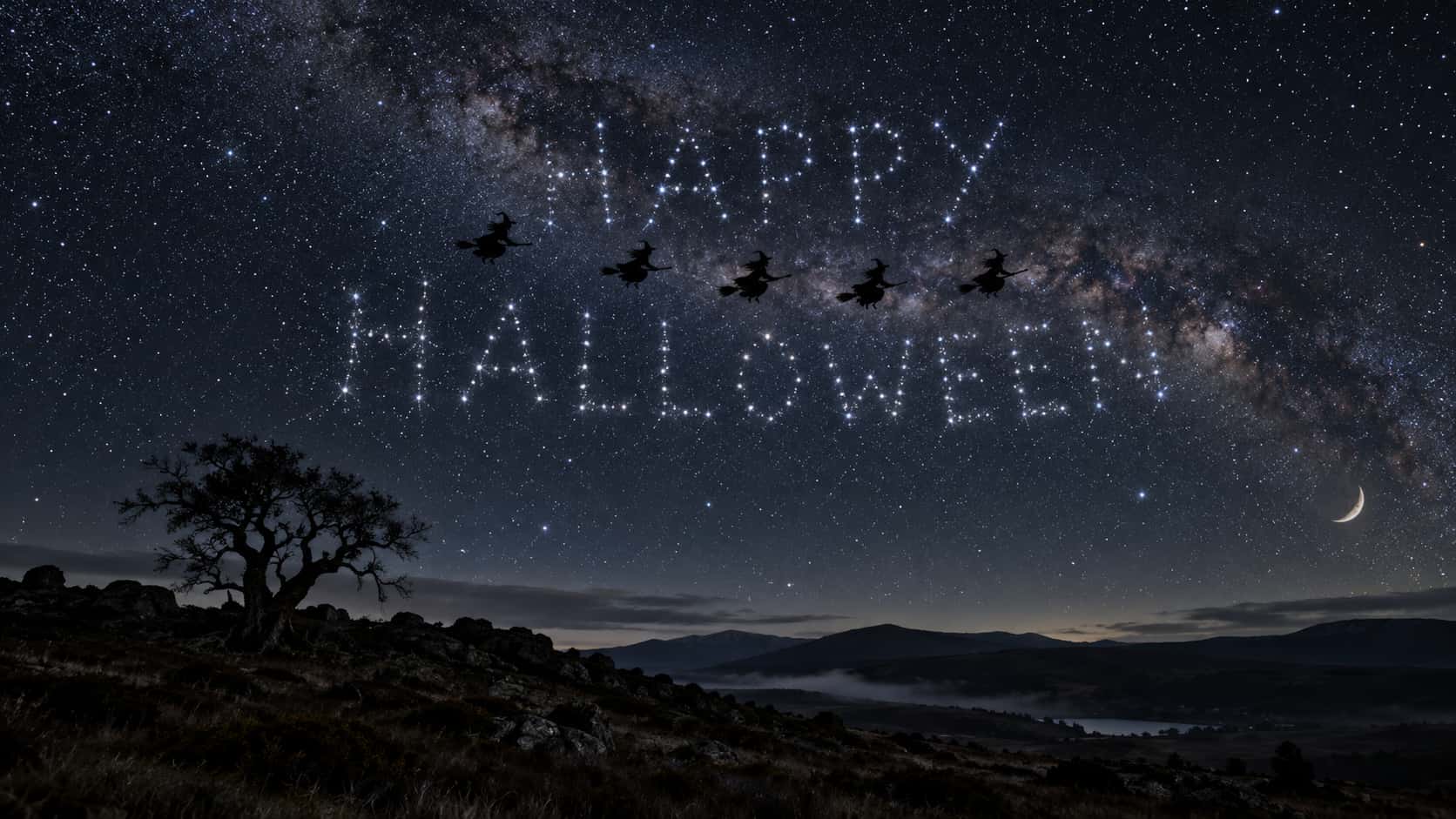 The words HAPPY above HALLOWEEN formed from bright star clusters in a night sky under the Milky Way, five black silhouettes of witches on broomsticks flying across them in a line and a thin crescent moon low at the right above a dark moorland ridge with a lone gnarled tree.
