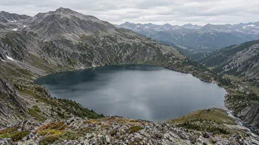 The whole mountain lake basin shows its oval shape from a high overlook with the shoreline ringed by slopes and the outlet notch at one end.