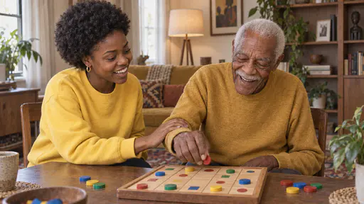 A young woman with a natural afro in a yellow sweatshirt gently guides the wrist of a tall elderly man in a mustard sweater who holds a counter toward the correct square on a board game while both laugh in bright afternoon light.