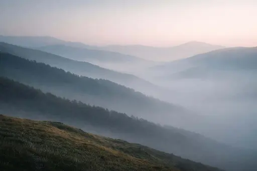 Layered hills shrouded in soft morning mist composed as a 3:2 landscape photograph with tonal depth, delicate pastel shifts and expansive negative space suitable for wallpaper.