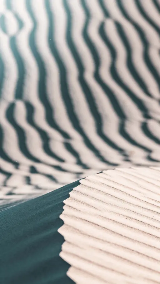 Close-up vertical 9:16 study of sand ripples filling the frame with diagonal curving bands of muted teal and soft off-white, shallow depth of field, matte granular texture.