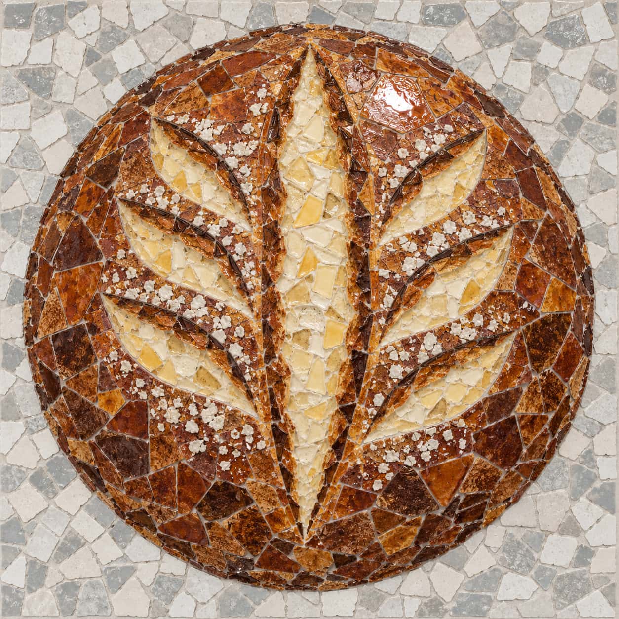 A mosaic of irregular glazed-tile shards showing a round sourdough loaf from above, its chestnut crust split along a central cut and curved side cuts into cream crumb, flecks of flour and a bright glaze highlight on a grey and white tile ground.