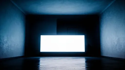 A low-key interior photograph of a dark room with a single illuminated screen as focal point, composed for a 16:9 wallpaper-style image with strong negative space.