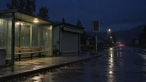 An empty small bus station at deep blue night has a shuttered kiosk with its striped awning rolled up, a green shelter lit by one lamp over a bare bench, a dark timetable board and the bus's rear lights fading down the far road.