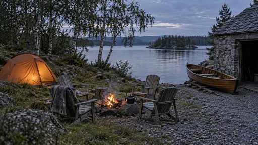 A lakeside plot at blue dusk has a small plain orange tent glowing from inside, a wooden rowing boat pulled up on a gravel slipway beside a stone boathouse and weathered garden chairs around a small camp fire with a kettle on a stone.
