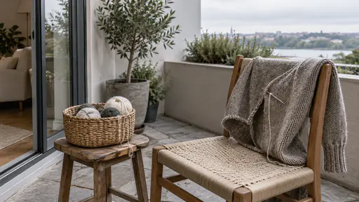 A terrace corner holds a plain sewing basket of thread balls on a small stool and a half mended plain jumper draped over a chair back.