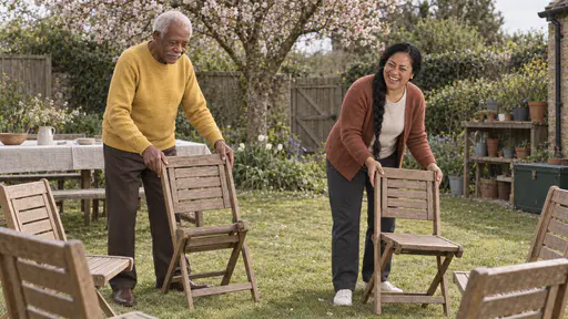 A tall elderly man with white hair and a white moustache in a mustard sweater and a woman with a long black braid in a rust cardigan unfold wooden garden chairs into a circle on a mown lawn in clear noon light.