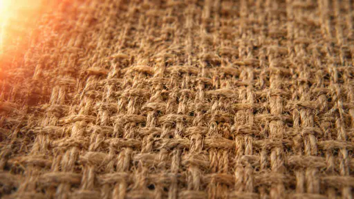 A wide close view of coarse woven jute in raw sienna and tan with the over under weave sharp and a soft amber film light leak across the upper left corner.